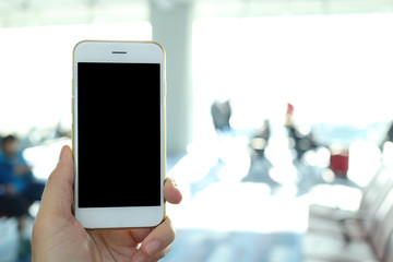 Poster - Hand holding mockup smartphone with airport passenger terminal background