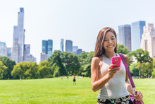Happy Asian Woman Texting Sms On Mobile Phone In New York City, NYC. Young Girl Walking In Central Park Meadow In Manhattan.