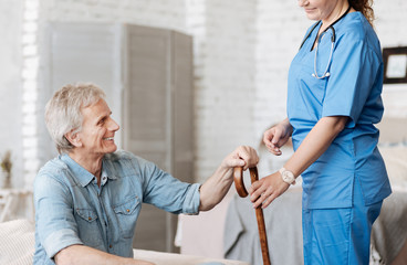 Wall Mural - Attentive experienced nurse bringing her patient his cane