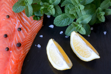 Wall Mural - Fresh salmon fillet with aromatic herbs, spices,  lemon on black stone background