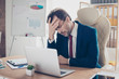 © deagreez - Depressed entrepreneur realtor is holding his head with hand, he is tired and frustrated, sitting in the office at his work place