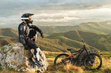 A Professional Downhill Rider Sits On A Stone Resting After A Tense Race On A Mtb Bike