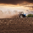 © LALSSTOCK - The tractor plows the field in the spring, and behind it the dust rolls and birds fly to find the food against the beautiful sunset sky. Agriculture