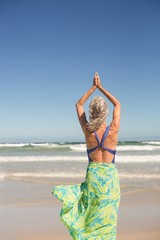 Wall Mural - Rear view of woman practising yoga while standing against sea