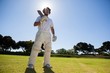 Confident player with cricket bat standing against sky