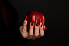Hands With Scary Nails Manicure Holding Poisoned Red Apple , Isolated On Black Background