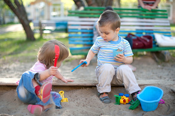 Two cute little children brother and sister playing in a sandbox