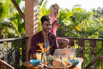 Poster - Couple Sitting On Summer Terrace Use Laptop Computer Having Breakfast Talking, Man And Woman In Morning Eating Outdoors With View On Tropical Forest