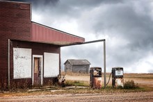 Horizontal Image Of A Very Old Abandoned Gas Station With Two Rusty Broken Down Gas Pumps Under A Dark Cloudy Thunder Storm.