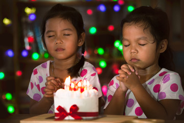 Happy twin two asian little girls make folded hand to wish the good things for their birthday in birthday party in dark tone