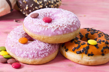 Wall Mural - Assortment of colorful donuts with candies on pink wooden background