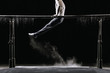 Male athlete performing handstand on gymnastic parallel bars with talcum powder. Isolated on black.