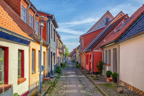 Fotografie, Obraz View down a historic cobble stone street with old colorful fishing cottages on a sunny day