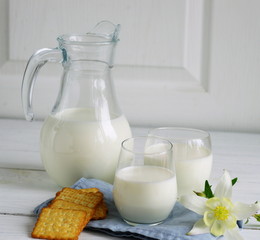 jug and glass of milk with a cookies on white wooden background