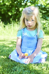 happy little child blond girl with lollipop resting on the grass in summer day