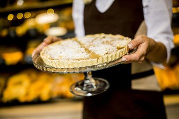 Bakery female worker posing with apple tart in bakery