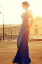 Fashion Full Length Portrait Of Elegant Beautiful Girl In Long Flying Waving Evening Blue Dress In City At Sunset            