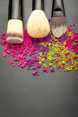 Above view on make-up brushes with colorful make-up eyeshadow on black texture with copy space