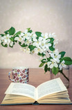 Fototapeta  - An open book on the table with a branch of apple blossoms and a cup of tea