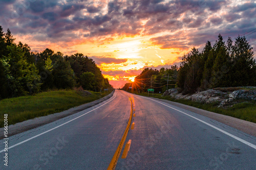 Sunset Rays Poking Through Trees On Open Country Road In