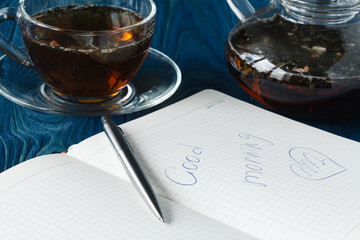 Wall Mural - Herbal tea in a glass transparent cup and open pure notebook