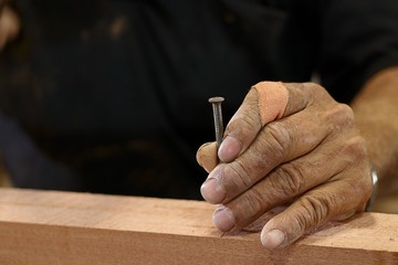 Hands senior carpenter holding nail on wooden piece with copy space.