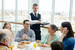 © pressmaster - Young waiter serving family in restaurant