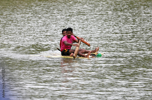 Two Boys Use Cricket Bats To Paddle A Handmade Boat On Flooded Two Boys Use Cricket Bats To Paddle A Handmade Boat On Flooded Road In