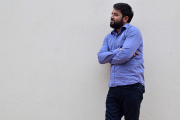 Handsome young bearded man standing against the wall, Portrait of bearded man with cross hands leaning against wall.