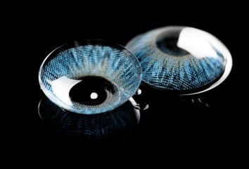 Blue contact lenses on wet black background with reflection