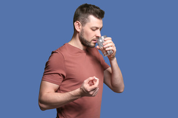 Sticker - Handsome young man taking pill on color background