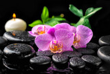 Fototapeta Łazienka - spa setting of blooming twig lilac orchid flower, green leaves with water drops, candle on zen basalt stones