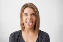 Disgusted Pretty Girl Sticking Out Tongue, Expressing Her Dislike Or Disregard Towards Something. Funny Humorous Young Woman Showing Tongue At Camera As If Teasing Someone, Having Playful Look