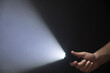 Black flashlight with a beam of light in male's hand isolated from right side of the frame on black background