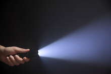 Black Flashlight With Wide Beam In Male's Hand Isolated From Left Side Of The Frame On Black Background
