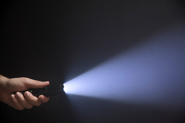 Black flashlight with wide beam in male's hand isolated from left side of the frame on black background