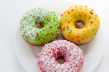 Wall Mural - Yellow, green and pink Donuts with polka dots on a plate on a white background. National Doughnut Day. Dessert food. Fried dough confectionery. Snacks.