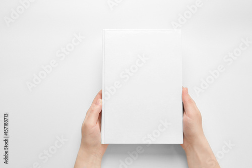 Fotografering Female hands holding closed book with blank cover on light background