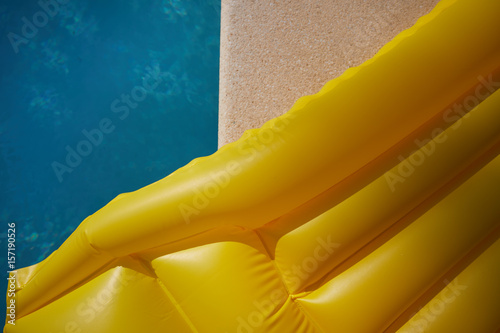 Fotografie, Obraz An inflatable yellow air mattress swimming in a shiny blue swimming pool