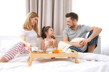 Happy family sitting on bed with breakfast