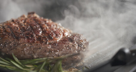 cooking rib eye steak with herbs on grill pan, wide photo