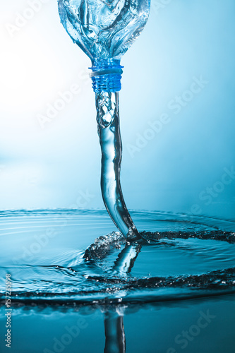 Naklejka dekoracyjna Water flow from a plastic bottle on blue background