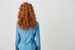 Photo of girl with red curly hair standing back to camera over white background. Copy space.