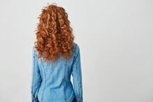Photo Of Girl With Red Curly Hair Standing Back To Camera Over White Background. Copy Space.