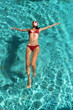 © antianti - A beautiful young slim sporty woman in a red bikini relaxes on azure water on a tropical island. Travel Concept