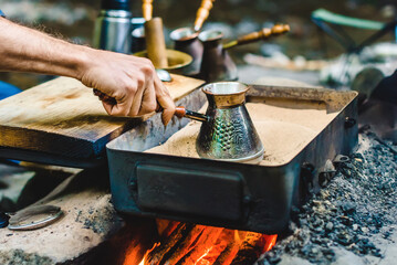 Man is cooking Turkish coffee in the box with sand under live coals