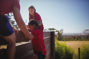 Wall Mural - trainer assisting kids to climb a wooden wall