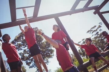 Wall Mural - trainer assisting kids to climb horizontal bar