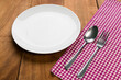 spoon and fork on tablecloth with white plate on wooden table