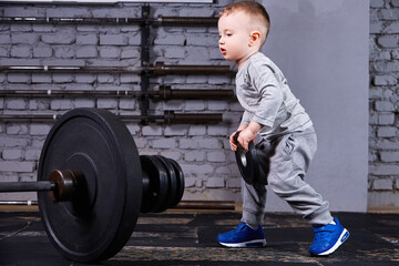 Little sporty child with barbbell against brick wall at the cross fit gym.